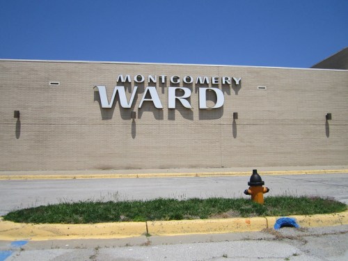 Sign for Montgomery Ward on a beige building, with a yellow fire hydrant and green grass in the foreground.