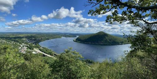 A scenic view of a river winding around a green hill, with blue skies and fluffy clouds above.