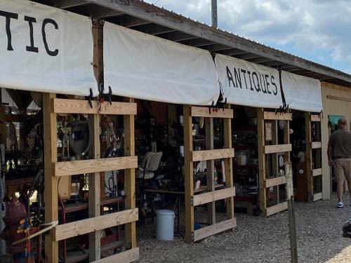 A rustic antique shop with wooden stalls, displaying various vintage items under a cloudy sky.