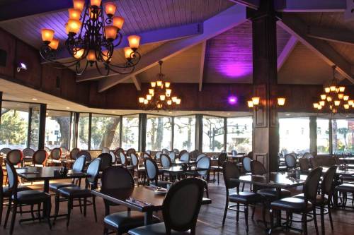 Interior of a restaurant featuring wooden beams, chandeliers, and empty tables with chairs in a warm, inviting atmosphere.
