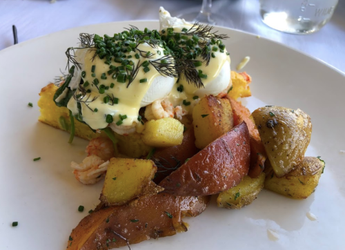 A plate of poached eggs on a bed of vegetables and herbs, served with roasted potatoes on the side.