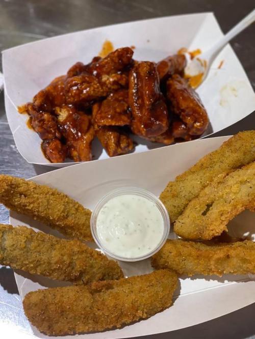 A tray with crispy fried pickles and a side of ranch dressing, alongside spicy chicken wings in sauce.