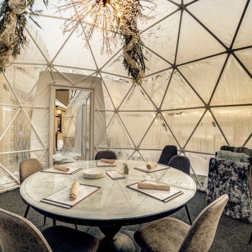 A modern geodesic dome interior featuring a round table set for dining, with elegant decor and a chandelier.