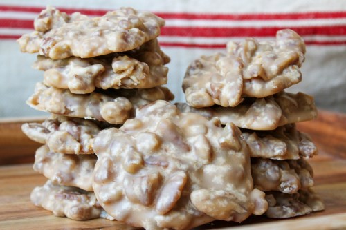 A stack of homemade praline cookies with a glossy, nutty coating on a wooden surface.