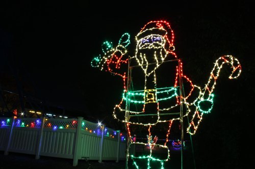 A large, illuminated Santa Claus figure waving, surrounded by colorful holiday lights at night.
