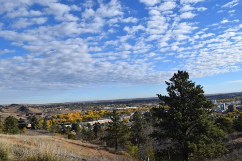 A panoramic view of a valley with colorful trees, rolling hills, and a blue sky filled with fluffy clouds.