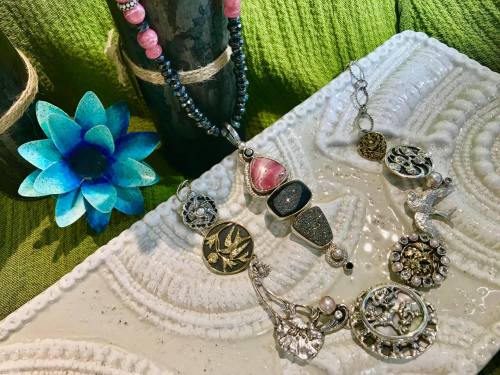 A collection of colorful jewelry pieces displayed on a textured surface, with a blue flower in the background.