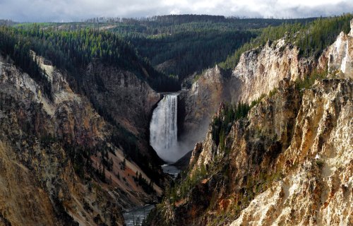 A stunning waterfall cascades down a rocky cliff, surrounded by lush green forests and rugged terrain.