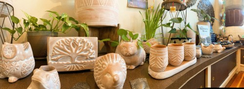 A display of handcrafted pottery, including animal figures and plant pots, surrounded by greenery on a wooden shelf.