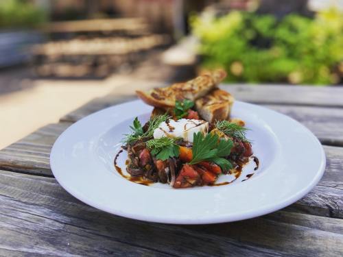 A plate of fresh salad topped with herbs and a poached egg, served with toasted bread on a wooden table outdoors.