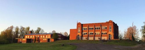 Historic brick buildings on a grassy hill, surrounded by trees under a clear blue sky during sunset.