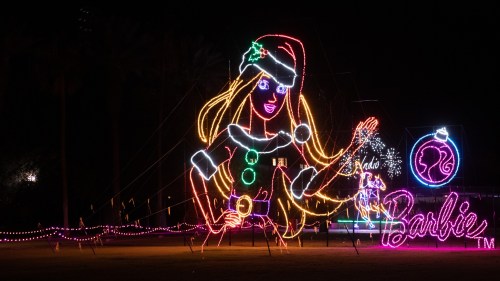A large, colorful light display of Barbie in a festive outfit, waving with a Christmas ornament nearby.