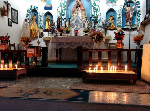 A small altar adorned with flowers, candles, and religious statues in a warmly lit space.