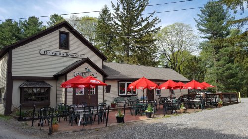 Exterior of The Vanilla Bean Café with outdoor seating under red umbrellas, surrounded by trees and gravel.