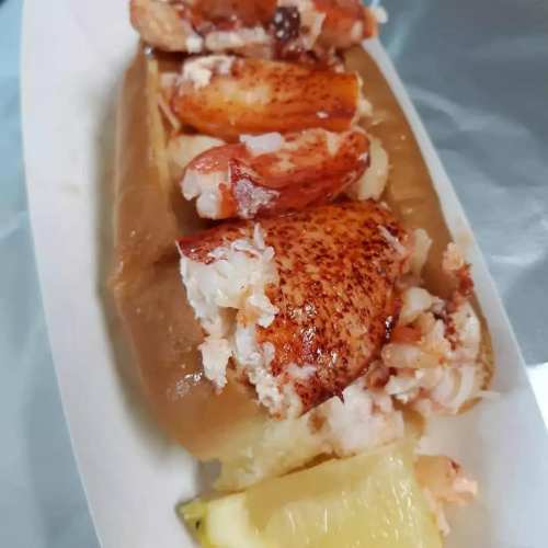 A lobster roll with chunks of lobster meat on a soft bun, served with a slice of lemon.