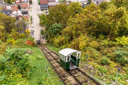 A funicular railway descends a hillside surrounded by trees, with a view of a town in the distance.