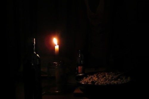 A dimly lit table with a candle, a bottle, and a bowl of food, creating a cozy, intimate atmosphere.
