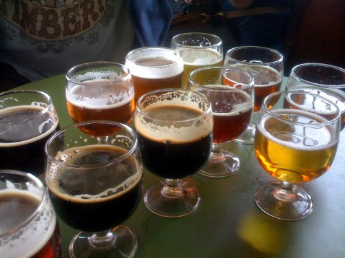A variety of craft beers in glasses, showcasing different colors and styles on a green table.