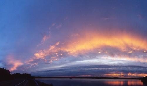 A panoramic view of a vibrant sunset over a calm lake, with colorful clouds reflecting in the water.