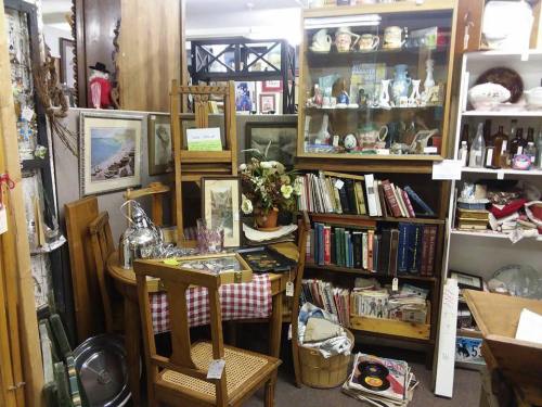 A cozy antique shop corner filled with vintage furniture, books, and decorative items on shelves and tables.