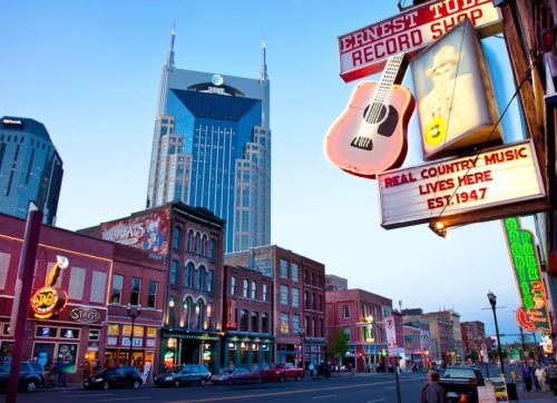 A vibrant street scene in Nashville featuring the Ernest Tubb Record Shop and colorful neon signs at dusk.