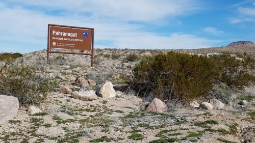 Sign for Pahranagat National Wildlife Refuge in a desert landscape with sparse vegetation and rocky terrain.