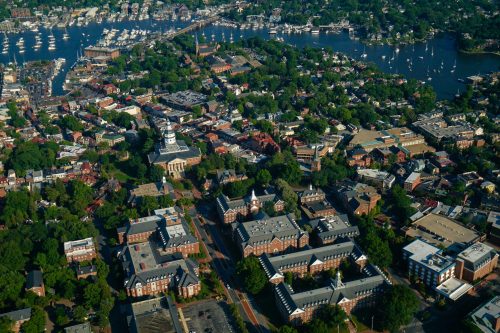 Aerial view of a coastal town with marinas, greenery, and historic buildings along the waterfront.