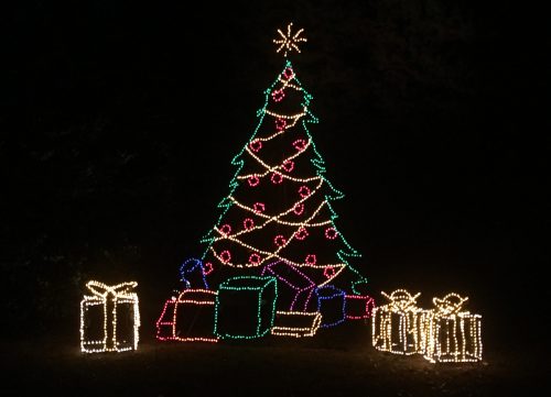 A brightly lit Christmas tree with colorful lights and presents underneath, set against a dark background.