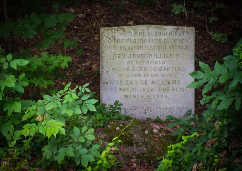 A weathered stone memorial in a wooded area, honoring Rev. John Williams and Mrs. Eunice Williams, with inscriptions.