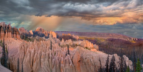 A panoramic view of rugged rock formations under a dramatic sky with clouds and soft sunlight illuminating the landscape.