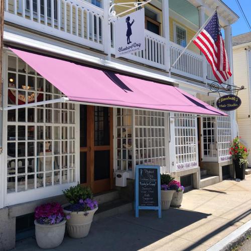 A quaint hair studio with a purple awning, American flag, and flower pots outside, showcasing a welcoming storefront.