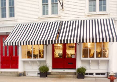 A storefront with a red door and large black-and-white striped awning, featuring large windows and potted plants.