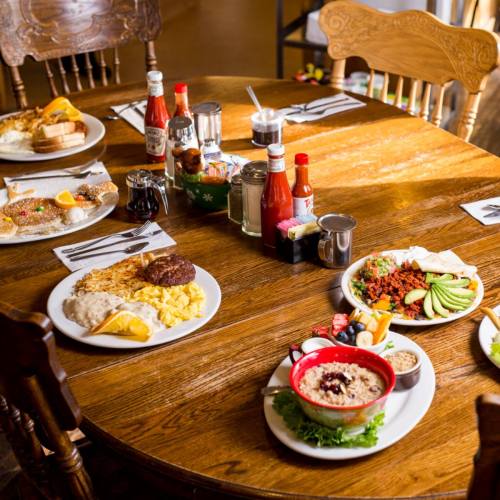A wooden table set with various breakfast dishes, including eggs, sausage, toast, and condiments.