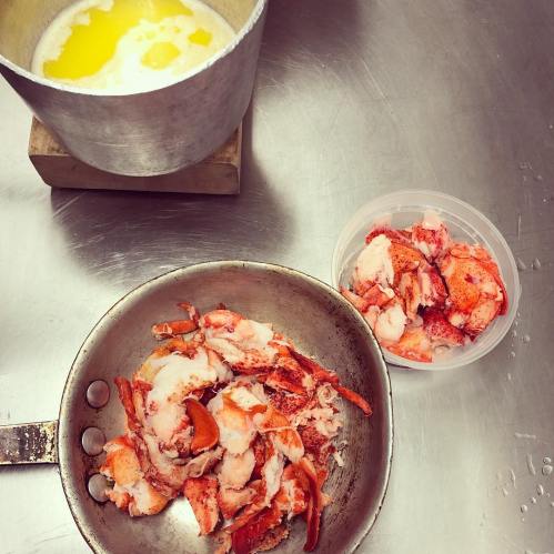 A pot of melted butter next to a skillet with lobster meat and a container of chopped lobster.