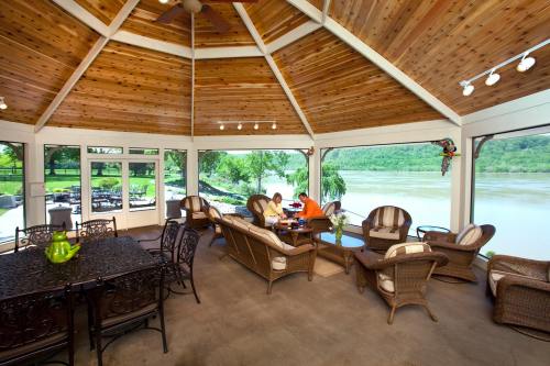 A cozy sunroom with wooden ceilings, seating, and a view of a river and greenery outside.