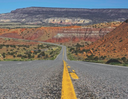 A winding road stretches through colorful desert landscapes with red and orange rock formations under a clear blue sky.