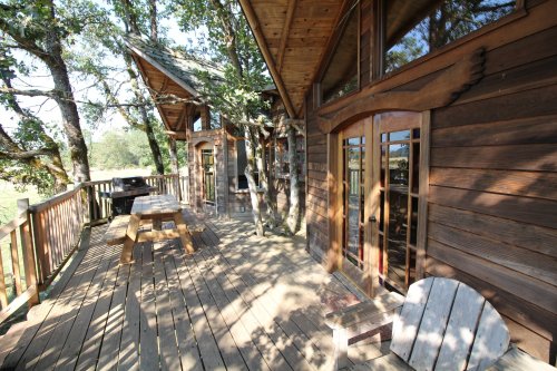 A wooden deck with a picnic table, surrounded by trees and featuring rustic cabin-style architecture.