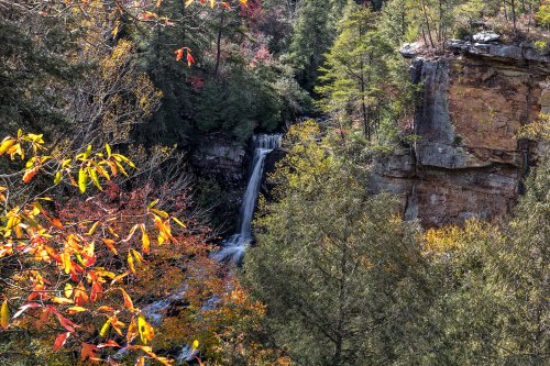 A scenic view of a waterfall surrounded by autumn foliage and rocky cliffs in a lush forest.