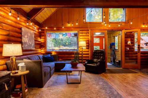 Cozy log cabin interior with warm lighting, a sofa, armchair, and decorative plants, creating a welcoming atmosphere.
