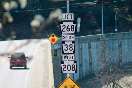 Road sign indicating junction for routes 268 South, 38 West, and 208, with a car approaching on the road.
