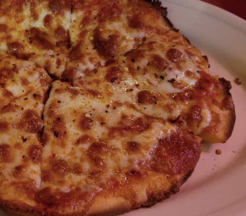 A close-up of a cheese pizza with golden, bubbly cheese and a crispy crust, sliced into eight pieces.