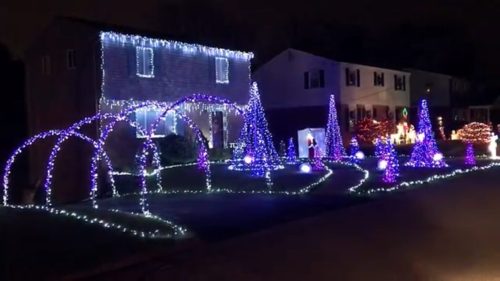 A festive display of colorful holiday lights adorning houses and trees in a nighttime neighborhood scene.