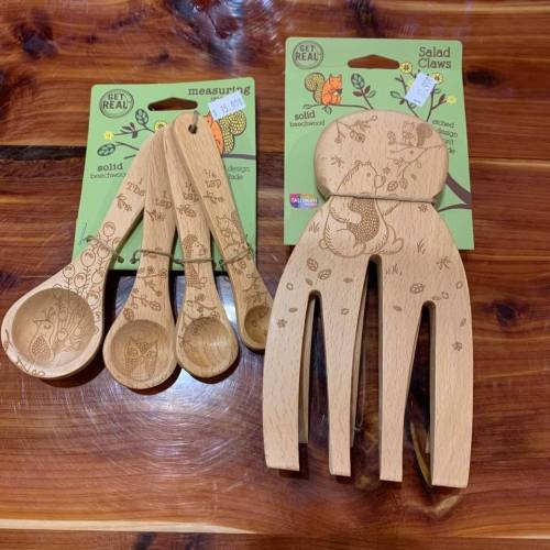 Two sets of wooden kitchen utensils: measuring spoons and salad claws, both with intricate designs, on a wooden surface.
