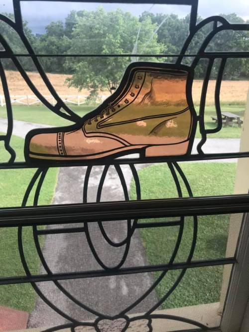 A decorative stained glass window featuring a large boot design, with a green landscape visible outside.