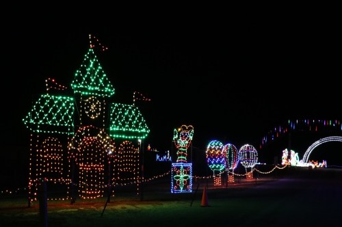 Colorful holiday lights illuminate a whimsical scene with a clock tower, balloons, and festive decorations at night.