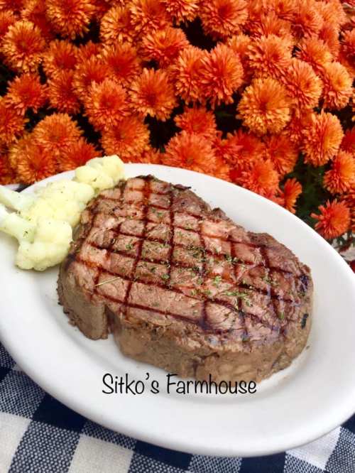 A grilled steak on a plate with cauliflower, set against a backdrop of vibrant orange flowers.