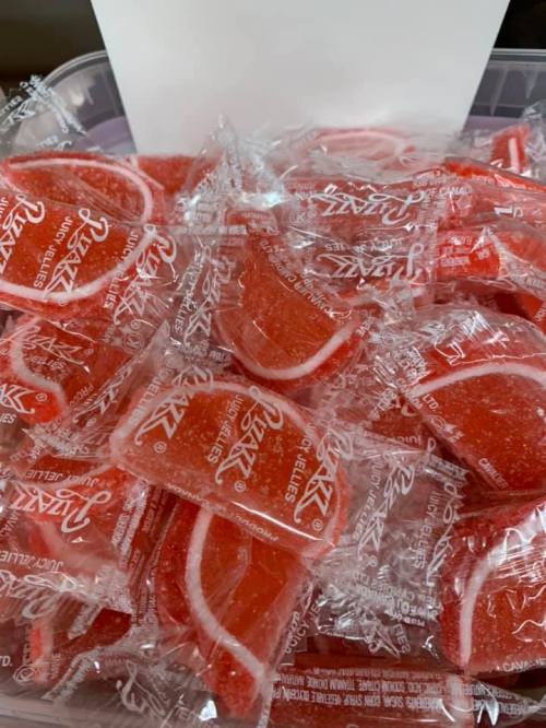 A container filled with individually wrapped red gummy candies shaped like slices of fruit.