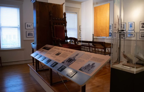A museum interior featuring a large chair, informational displays about historic architecture, and framed photographs on the walls.