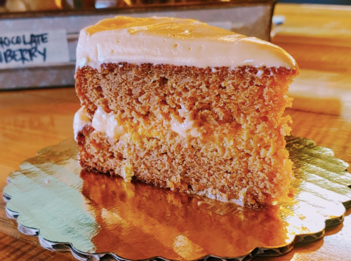 A slice of moist cake with creamy frosting on top, displayed on a golden plate.