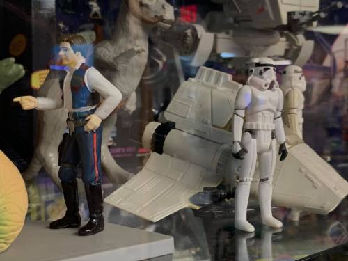 A Han Solo action figure stands next to a Stormtrooper and a miniature spacecraft in a display case.